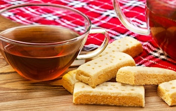 a cup of tea in a clear glass cup next to 6 shortbread fingers laid over a red tartan blanket 