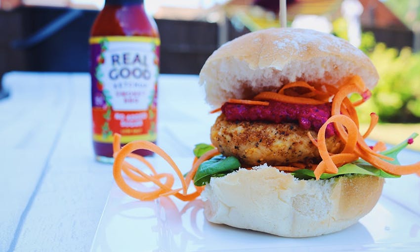 chicken burger with fresh lettuce and salad inside a fluffy white burger bun with smokey bbq real good ketchup on a white wooden bench 