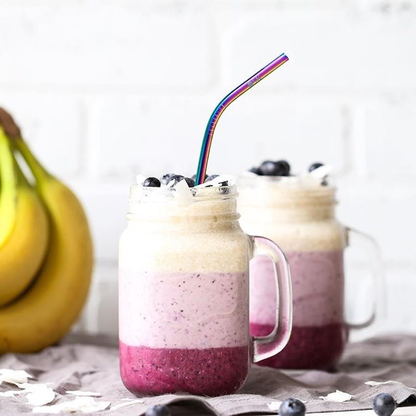 three tiered dark pink pale pink and cream smoothies in a jar topped with blueberries with OSK Eco metallic rainbow straw 