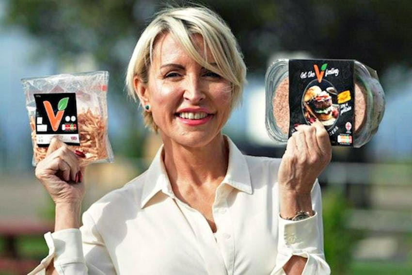 Heather mills smiling whilst holding vbites products in each hand infront of a farmyard background 