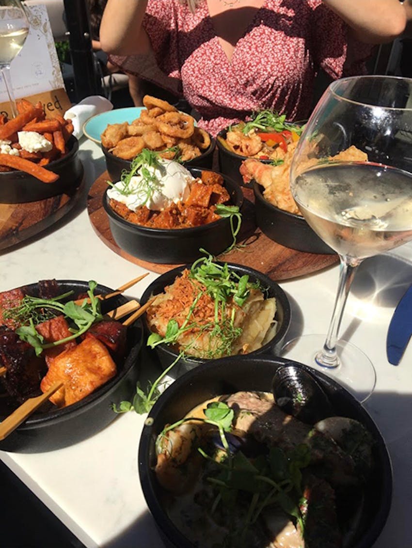 eight small tapas dishes in black bowls accompanied by two glasses of wine 