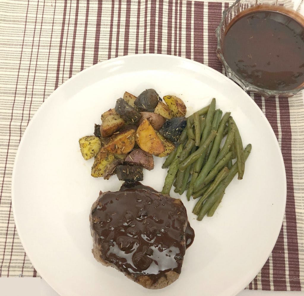a white plate with steak covered in chocolate and coffee sauce, green beans and roasted vegetables 