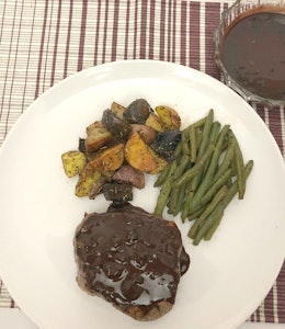 a white plate with steak covered in chocolate and coffee sauce, green beans and roasted vegetables 