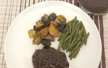 a white plate with steak covered in chocolate and coffee sauce, green beans and roasted vegetables 