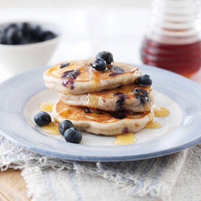 a stack of three pancakes topped with fresh blueberries and drizzled with maple syrup  