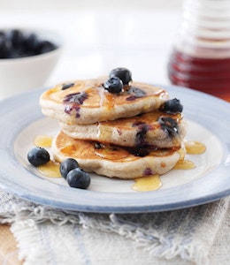 a stack of three pancakes topped with fresh blueberries and drizzled with maple syrup  