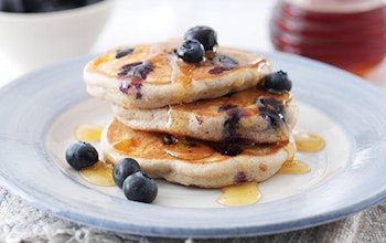a stack of three pancakes topped with fresh blueberries and drizzled with maple syrup  