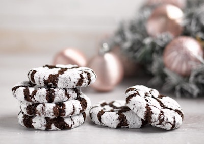 a pile of six brown and white festive cookies infront of a frosted white christmas tree decorated with gold baubles 