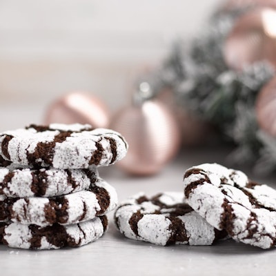 a pile of six brown and white festive cookies infront of a frosted white christmas tree decorated with gold baubles 