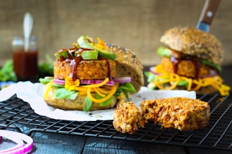two burger buns filled with lentil and mixed seeds burgers, avocado, sauce and salad on a wire cooling rack 