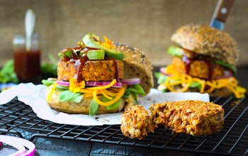 two burger buns filled with lentil and mixed seeds burgers, avocado, sauce and salad on a wire cooling rack 