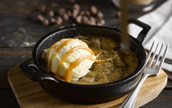 Baker & Baker Warm Cookie Dough Dessert black skillet with warm cookie dough with a scoop of vanilla ice cream and chocolate sauce drizzled on top