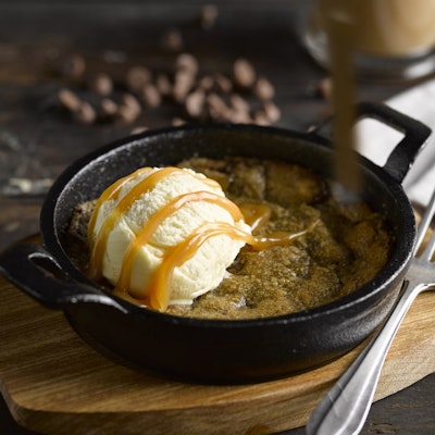 black skillet with warm cookie dough with a scoop of vanilla ice cream and chocolate sauce drizzled on top 
