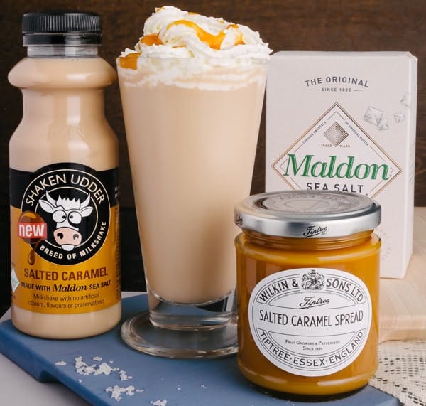 Ingredients for the Shaken Udder Salted Caramel Hot Chocolate shaken udder salted caramel milkshake and wilkin and sons salted caramel spread next to a tall glass of salted caramel hot chocolate