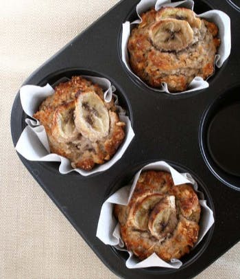 Three golden brown cooked banana muffins in a muffin tray lined with baking paper