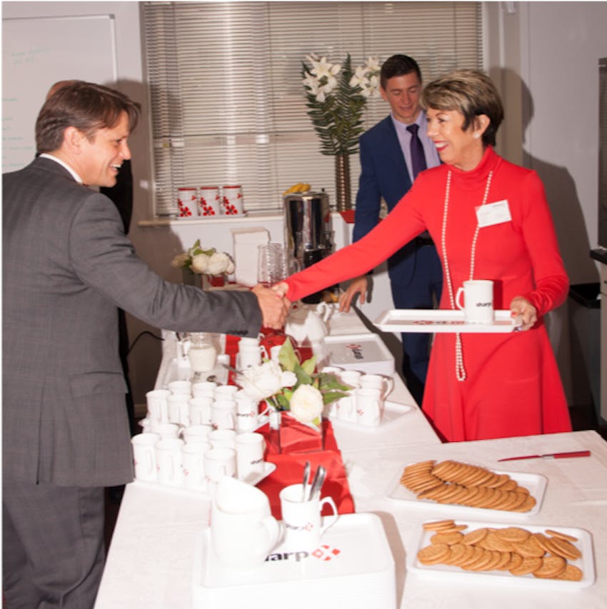 Jean Freeman shaking hands with a man in a grey suit over a long table filled with teacups and biscuits 