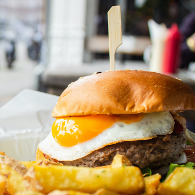 street food plate of crispy golden chips and a beef burger with a fried egg and a golden crisp bun 