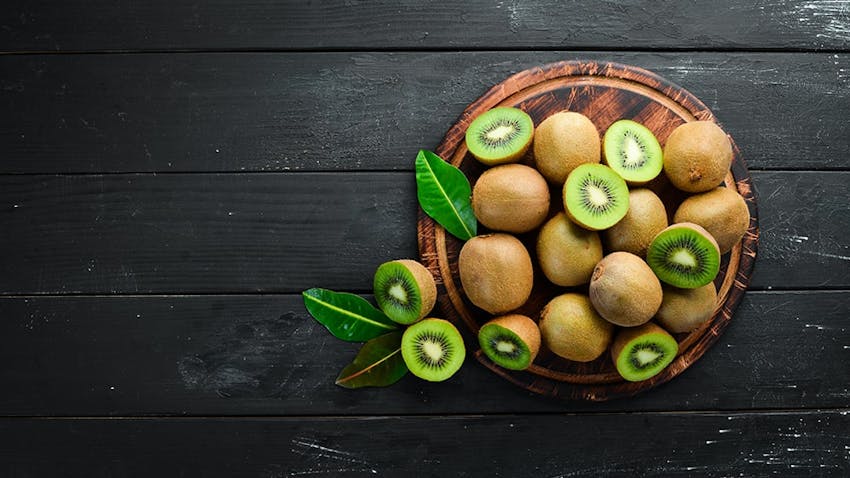 birds eye view of a wooden chopping board topped with whole and halved fresh kiwis