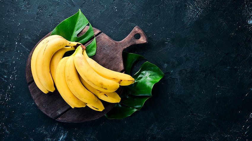 a bunch of yellow bananas on a wooden circular chopping board placed on banana leaf