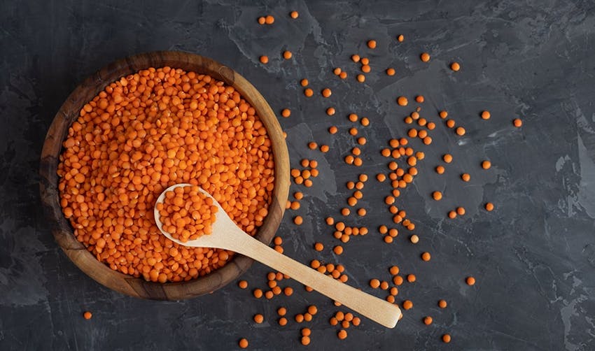 wooden bowl filled with orange dried uncooked lentils 