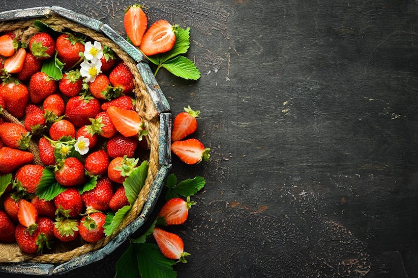 a punnet filled with red strawberries halved strawberries and mint leaves