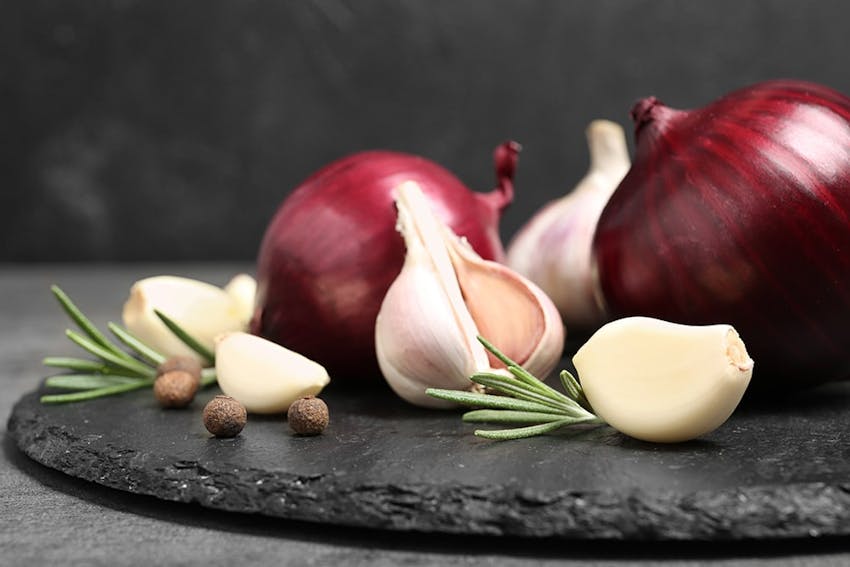  red onions garlic bulbs and garlic cloves with peppercorns and rosemary on a dark stone slate