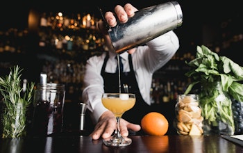 bartender holds a cocktail shaker over a half serve glass pouring in an alcoholic drink