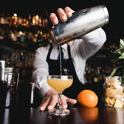 Allergens can easily hide in cocktails bartender holds a cocktail shaker over a half serve glass pouring in an alcoholic drink