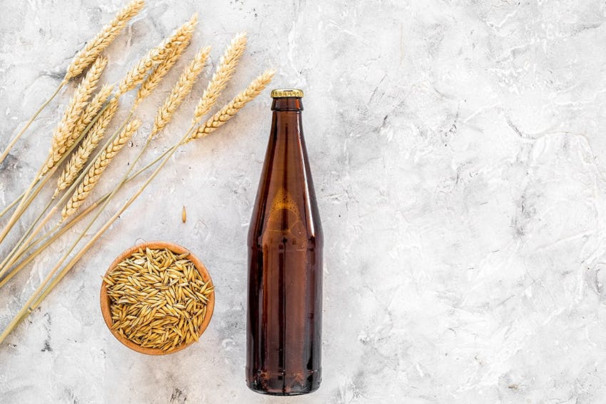 a bottle of beer on a white marble worktop next to a bowl of wheat grains and stalks of wheat