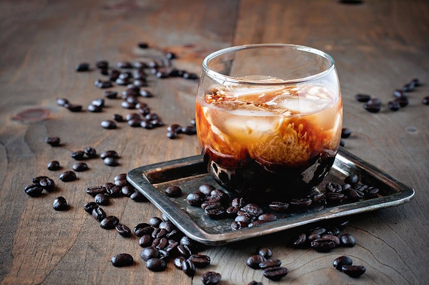 a small glass filled with kahlua on a metal tray surrounded by scattered coffee beans