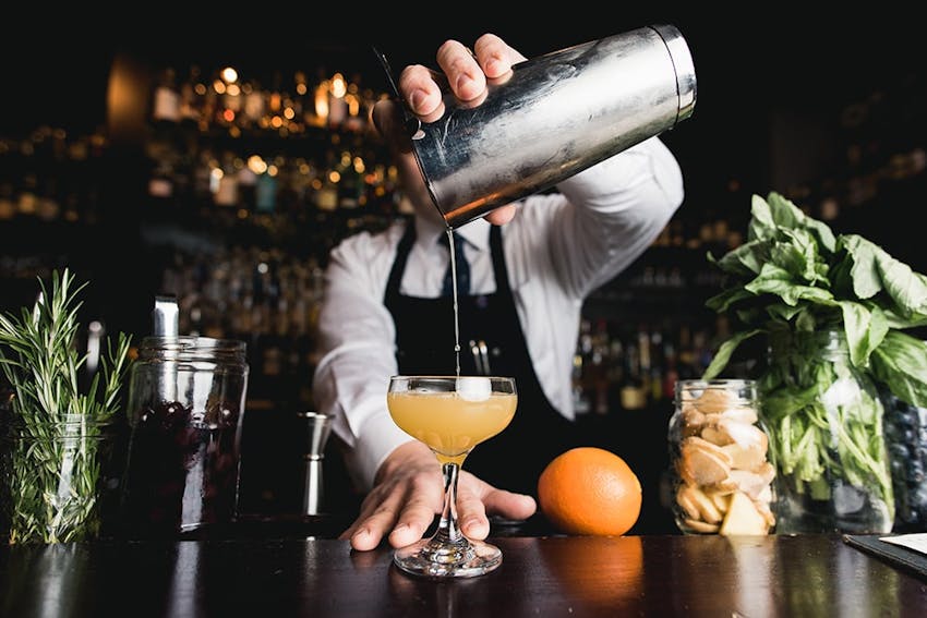 bartender holds a cocktail shaker over a half serve glass pouring in an alcoholic drink