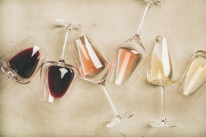 six wine glasses containing red white and rose creatively lined up in different angles on a white tablecloth 