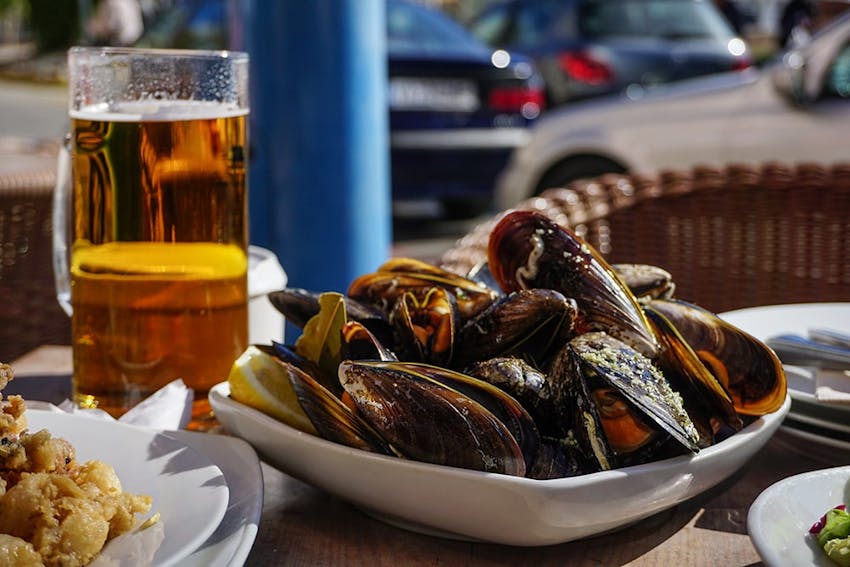 a bowl of oysters next to a pint glass of beer on an outdoor dining table 