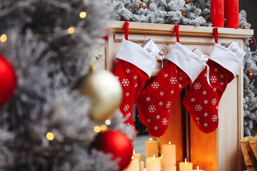 Be careful when choosing stocking fillers for allergens! three red christmas stockings hung on the fireplace above candles next to a frosted christmas tree with red and gold baubles