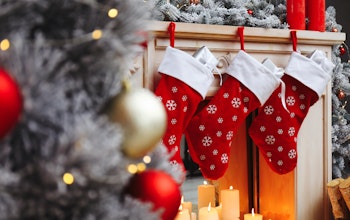 three red christmas stockings hung on the fireplace above candles next to a frosted christmas tree with red and gold baubles 