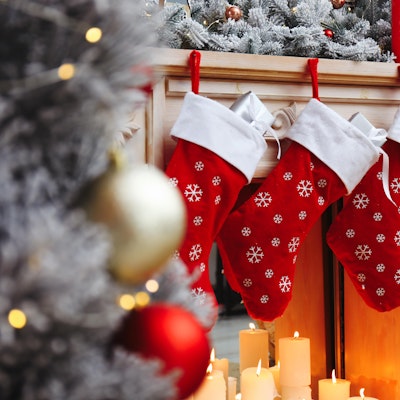 three red christmas stockings hung on the fireplace above candles next to a frosted christmas tree with red and gold baubles 
