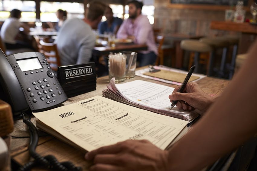 restaurant desk with phone reserved signs and woman leant over a list of menus writing down allergen information 