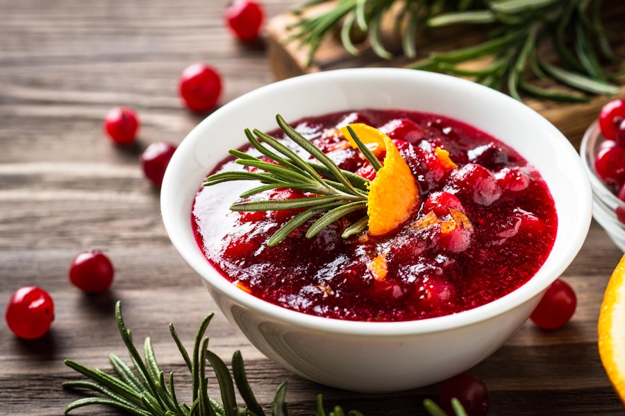 a small white bowl of cranberry sauce topped with rosemary and a slice of orange peel