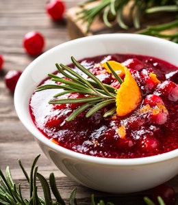 a small white bowl of cranberry sauce topped with rosemary and a slice of orange peel
