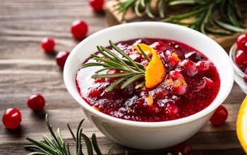 a small white bowl of cranberry sauce topped with rosemary and a slice of orange peel