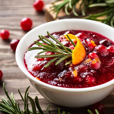 Cranberry Sauce a small white bowl of cranberry sauce topped with rosemary and a slice of orange peel