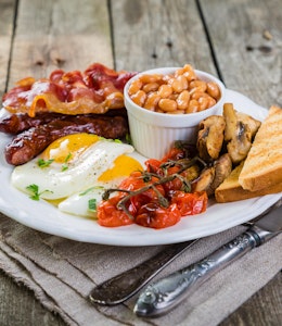 big english breakfast consisting of a pot of baked beans, brown bread, vine tomatoes, mushrooms, eggs, bacon and sausages 