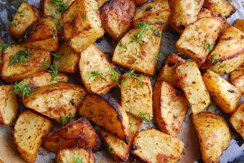 a baking tray of crispy roast potatoes topped with herbs 