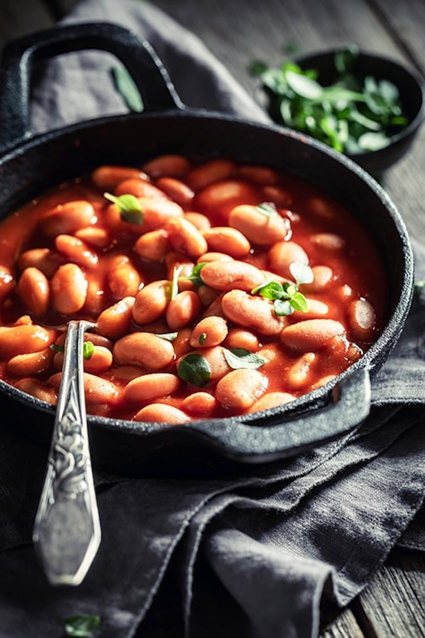 an iron skillet filled with baked beans topped with fresh herbs 