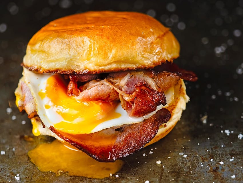 crispy bacon and a runny egg in a toasted golden bun with egg yolk oozing down the side of the bun 