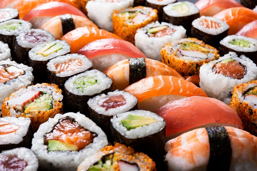 a dark brown circular bowl filled neatly with a range of different types of sushi, maki, sashimi, nigri on top of a dark marble table 