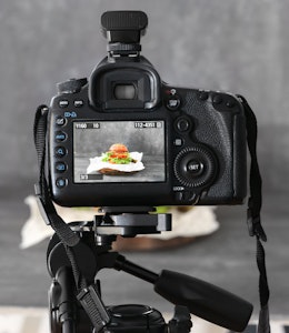 a dslr camera on a tripod shooting a burger on a grey backdrop