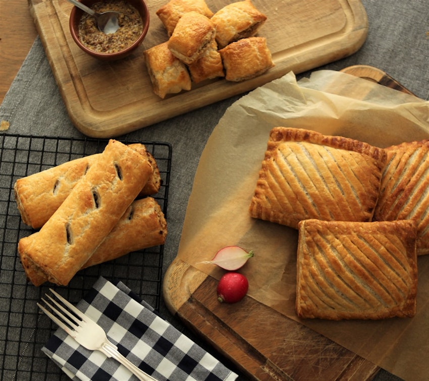 a range of fields and forest foods freshly baked sausage rolls, mini sausage rolls, and pasties on cooling racks and wooden chopping boards