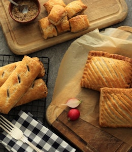 a range of fields and forest foods freshly baked sausage rolls, mini sausage rolls, and pasties on cooling racks and wooden chopping boards