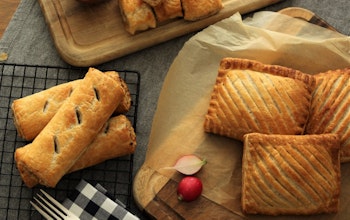 a range of fields and forest foods freshly baked sausage rolls, mini sausage rolls, and pasties on cooling racks and wooden chopping boards